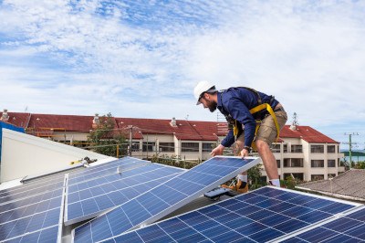 Auf Hausdach steht ein Monteur mit PV-Panel in den Händen.